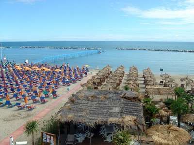 Spiaggia con file di ombrelloni colorati e capanne di paglia vicino al mare.