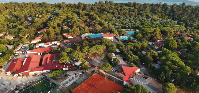Vista aerea di un villaggio turistico tra alberi e campi sportivi.