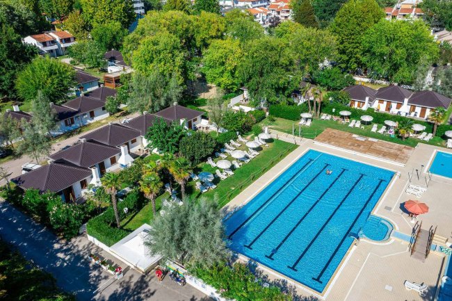 Vista aerea di piscina e bungalow tra alberi.