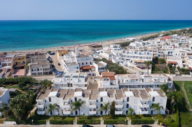 Vista aerea di una città costiera con edifici bianchi e mare turchese.