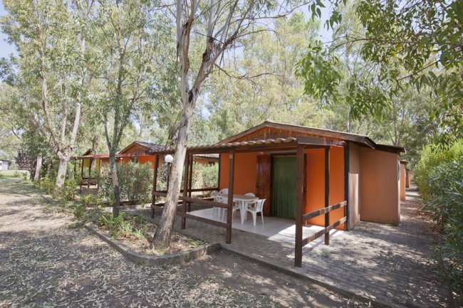 Bungalow arancione con veranda tra alberi.