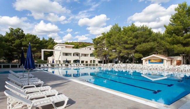 Piscina grande circondata da lettini bianchi.