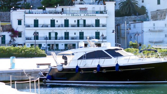 Un hotel bianco fronte mare con una barca ormeggiata davanti.