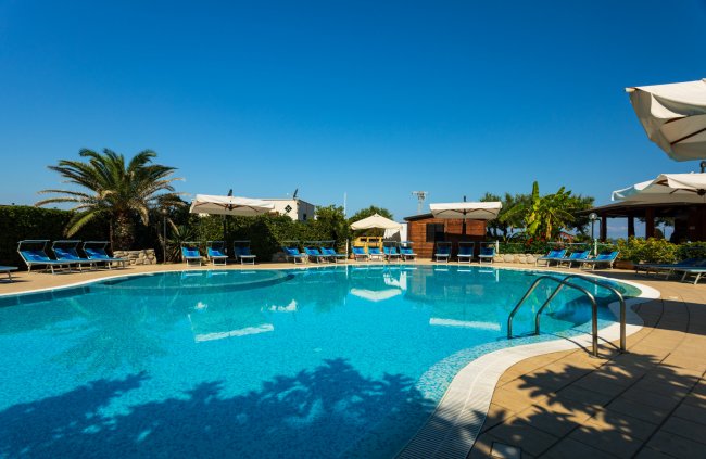 Piscina con ombrelloni e lettini blu sotto un cielo limpido.