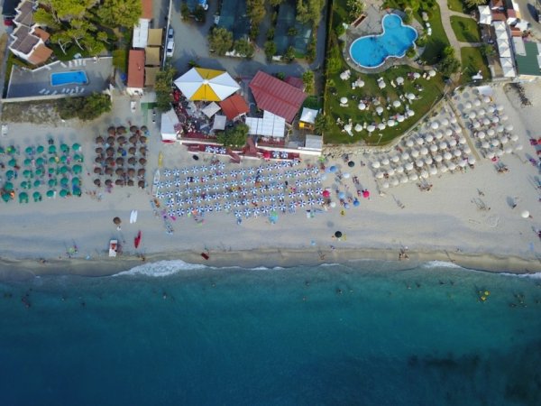 Vista aerea di spiaggia con ombrelloni e piscina vicina.