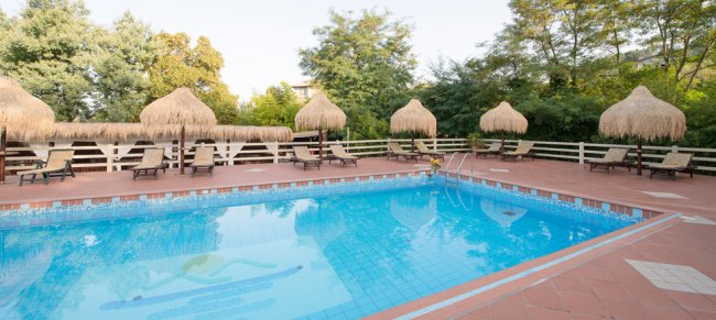 Piscina esterna con lettini e ombrelloni di paglia.