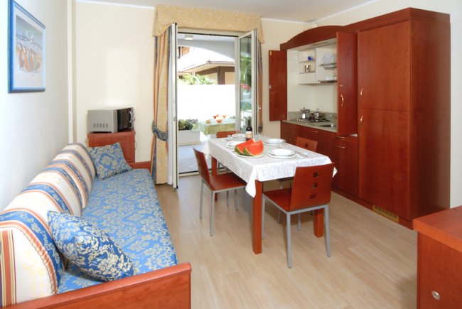 Soggiorno luminoso con divano, tavolo e cucina a vista.