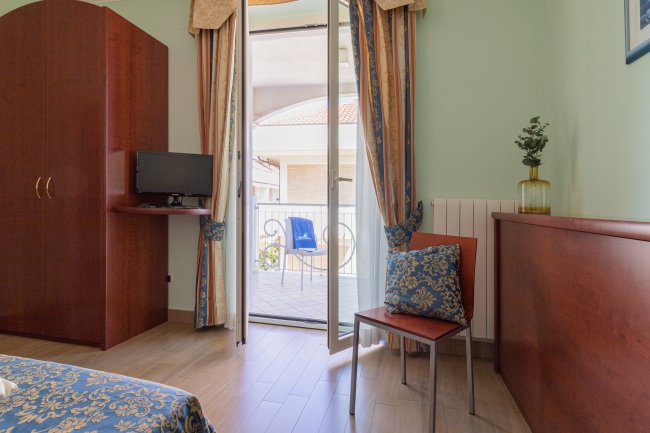 Stanza con balcone e tende, sedia con cuscino decorativo.