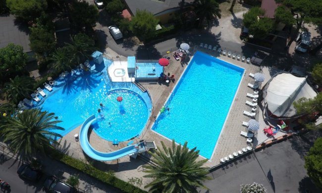 Vista dall'alto di due piscine, uno scivolo e lettini intorno.