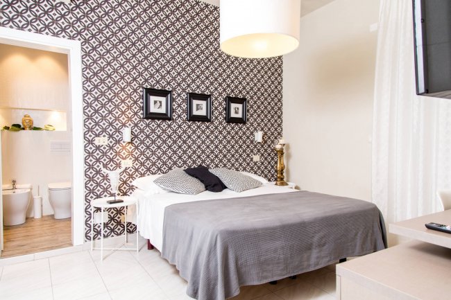 Camera con parete a pattern, letto, quadri e bagno annesso.