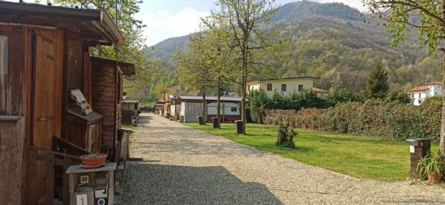 Stradina ghiaiosa tra casette di legno e alberi, montagne sullo sfondo.