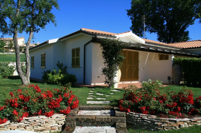Un bungalow bianco con giardino e fiori rossi.