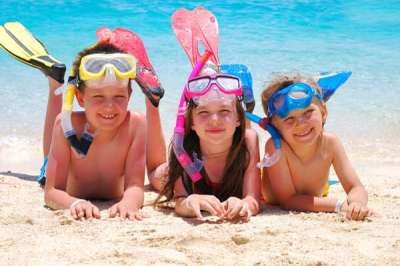 Tre bambini con maschere da snorkeling sdraiati sulla spiaggia.