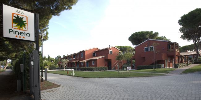 Un complesso di edifici in muratura rossa con alberi, strada e un cartello