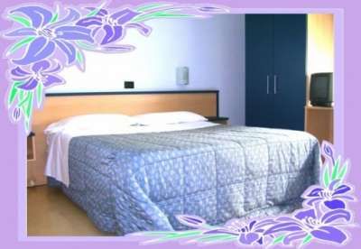 Camera d'albergo con letto matrimoniale e copriletto blu, contornata da cornice floreale viola.