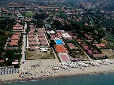 Vista aerea di un resort sulla spiaggia con edifici, piscina e ombrelloni.