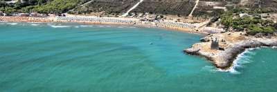 Spiaggia con mare blu e una torre su una scogliera.