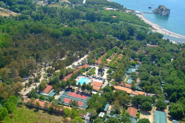 Veduta aerea di un campeggio con piscina e campi sportivi vicino al mare.