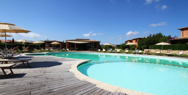 Piscina con sdraio e ombrelloni sotto un cielo blu.
