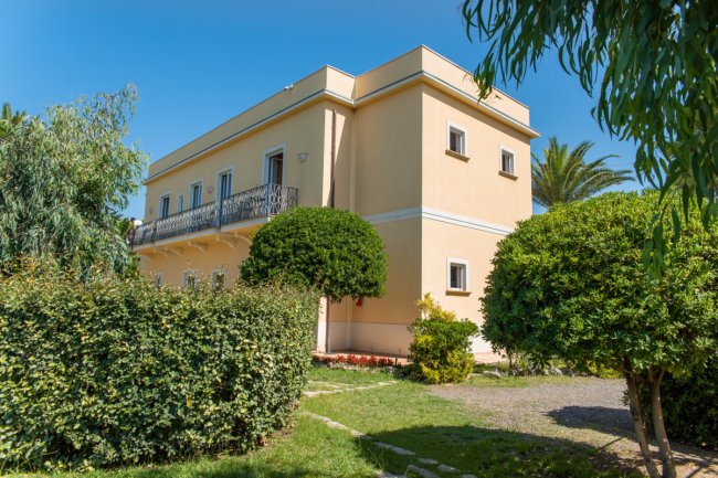 Edificio beige a due piani circondato da siepi.
