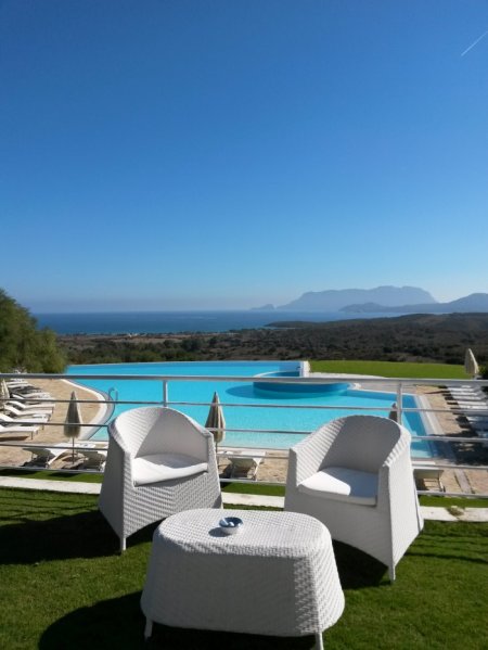 Due sedie bianche di fronte a una piscina con vista mare.