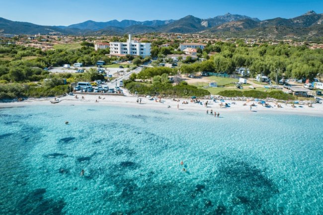 Spiaggia con mare cristallino e colline sullo sfondo.
