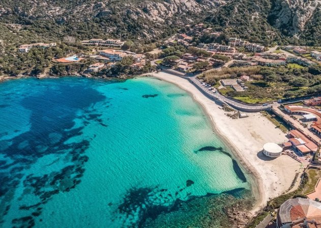 Spiaggia con mare azzurro e villette immerse nella natura.