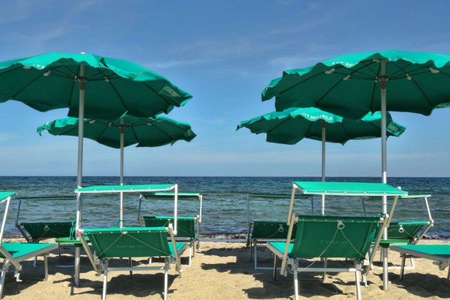 Spiaggia con ombrelloni verdi e lettini.