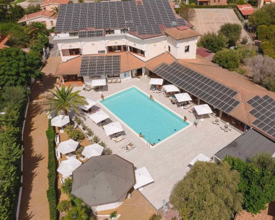 Piscina circondata da ombrelloni e lettini, edificio con pannelli solari sopra.