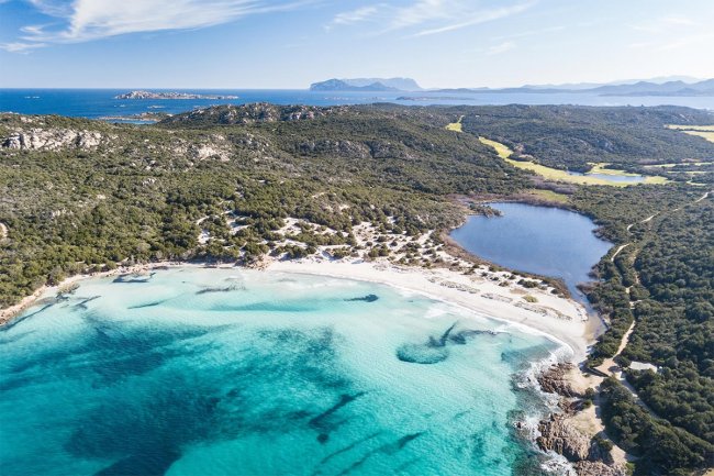 Spiaggia con mare turchese e colline verdi.