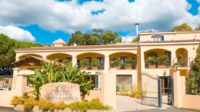 Edificio hotel giallo con vegetazione circostante.