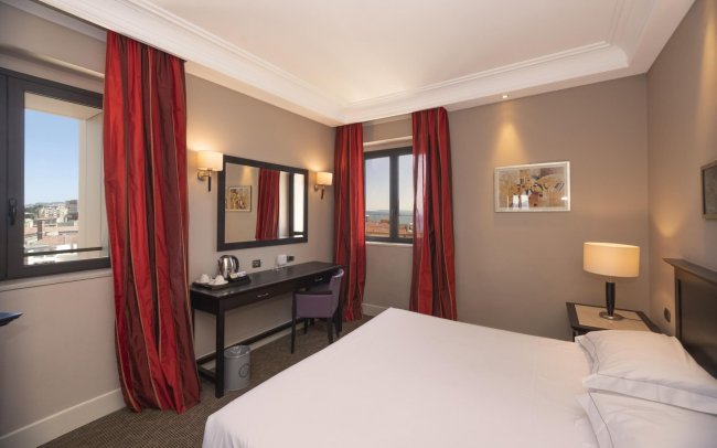 Camera d'hotel con letto matrimoniale e tende rosse.