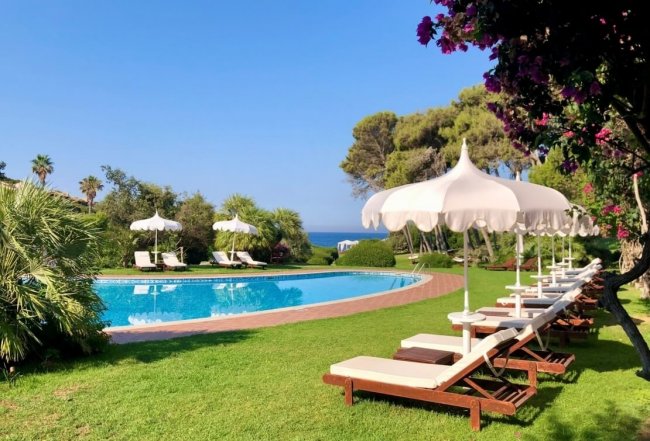 Piscina con lettini e ombrelloni bianchi su prato verde.