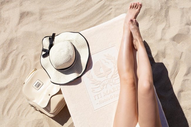 Gambe abbronzate sulla spiaggia con cappello e borsa.