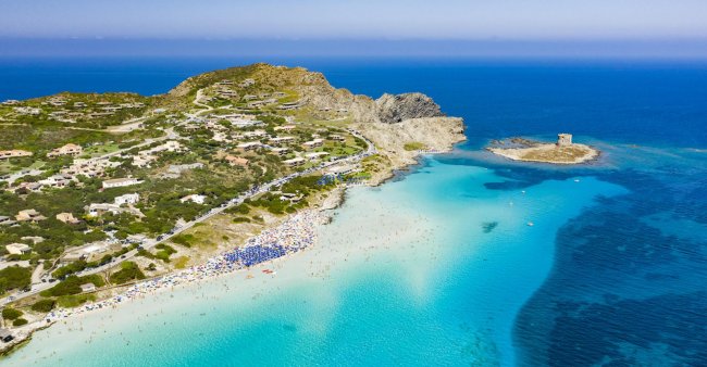 Spiaggia con acque turchesi e una torre su un isolotto.