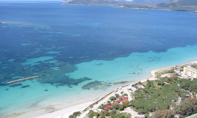 Spiaggia sabbiosa con mare turchese e colline.