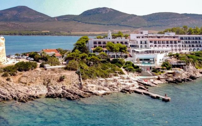 Hotel su scogliera con mare e montagne sullo sfondo.