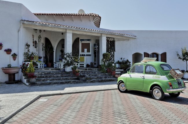 Casa bianca con auto verde davanti.
