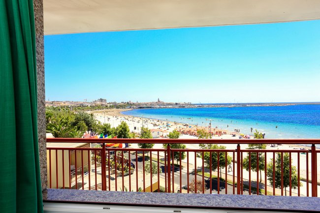 Balcone con vista su spiaggia affollata e mare blu.