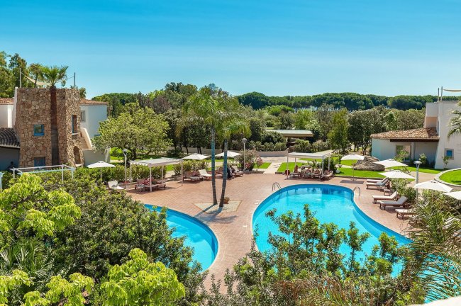 Piscina a forma di otto circondata da lettini e vegetazione.