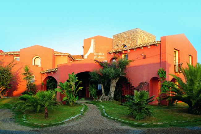 Edificio rosso con archi, palme e giardino anteriore.