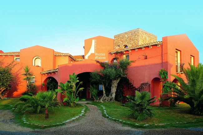 Edificio rosso con palme e piante.
