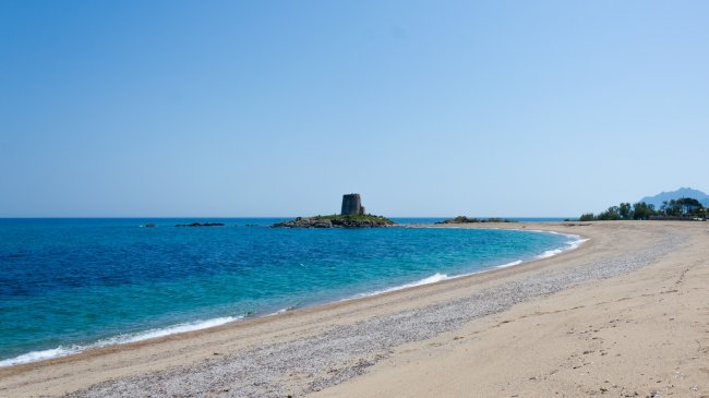 Spiaggia con torre sul mare e sabbia dorata.