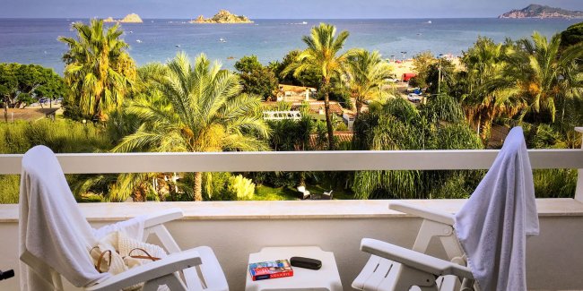 Balcone con sedie e vista mare, palme e isole.