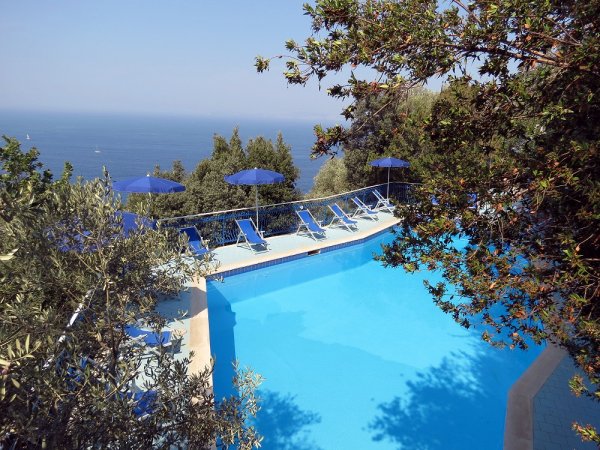 Piscina blu vista mare con sdraio e ombrelloni.