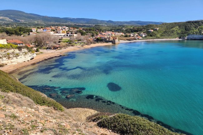 Baia con acqua turchese e villaggio sullo sfondo.