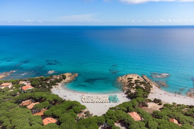 Spiaggia dall'alto con ombrelloni bianchi e mare azzurro.