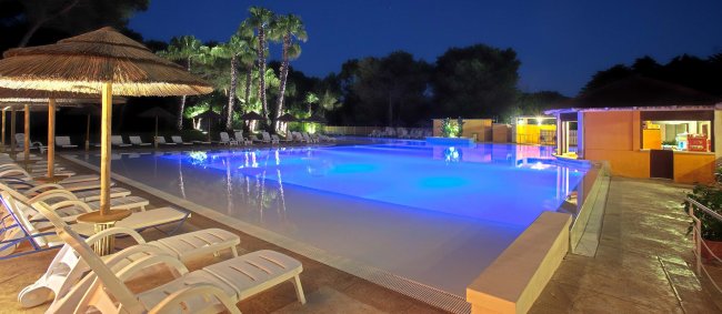 Piscina illuminata di notte con lettini.