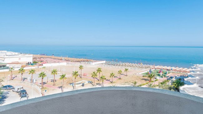 Spiaggia attrezzata, mare azzurro e palme viste dall'alto.