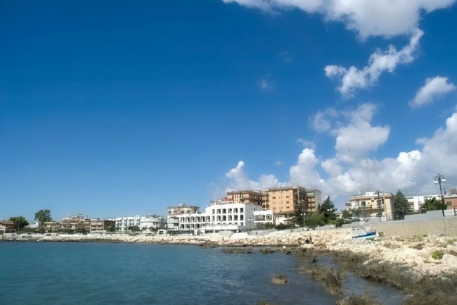 Costa rocciosa con edifici bianchi e cielo blu.